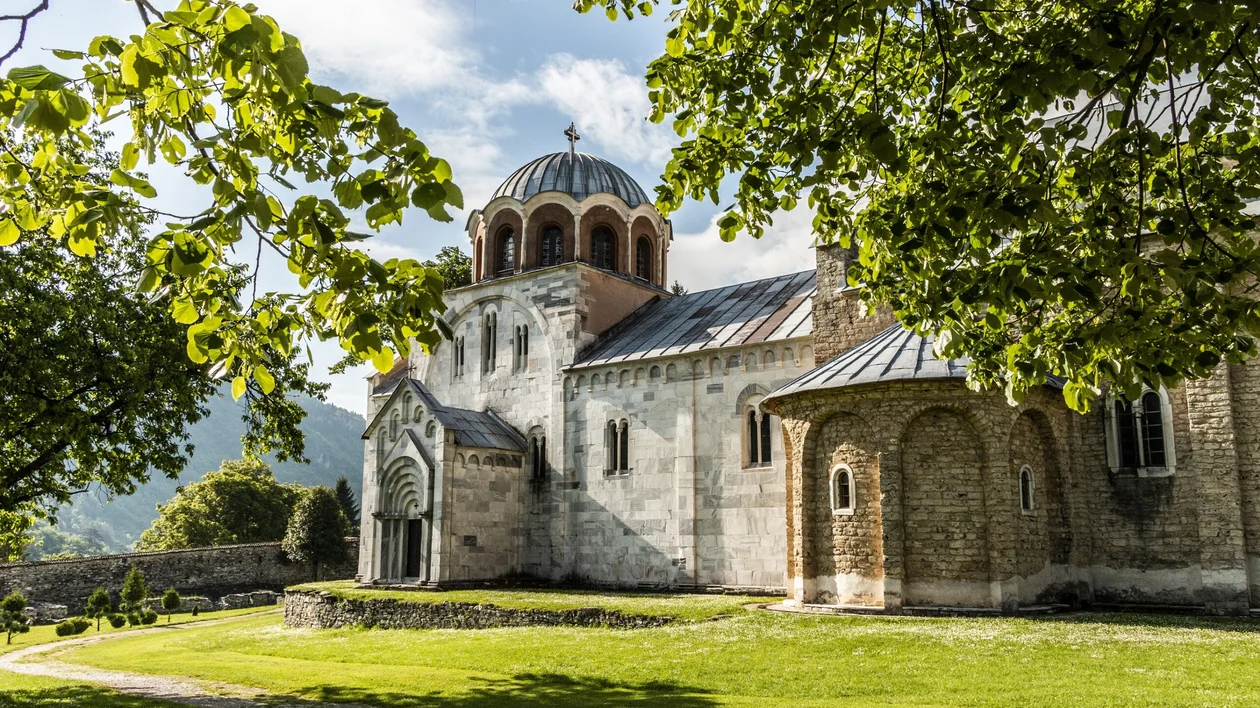 Stone church with a dome, surrounded by trees and green grass on a sunny day.