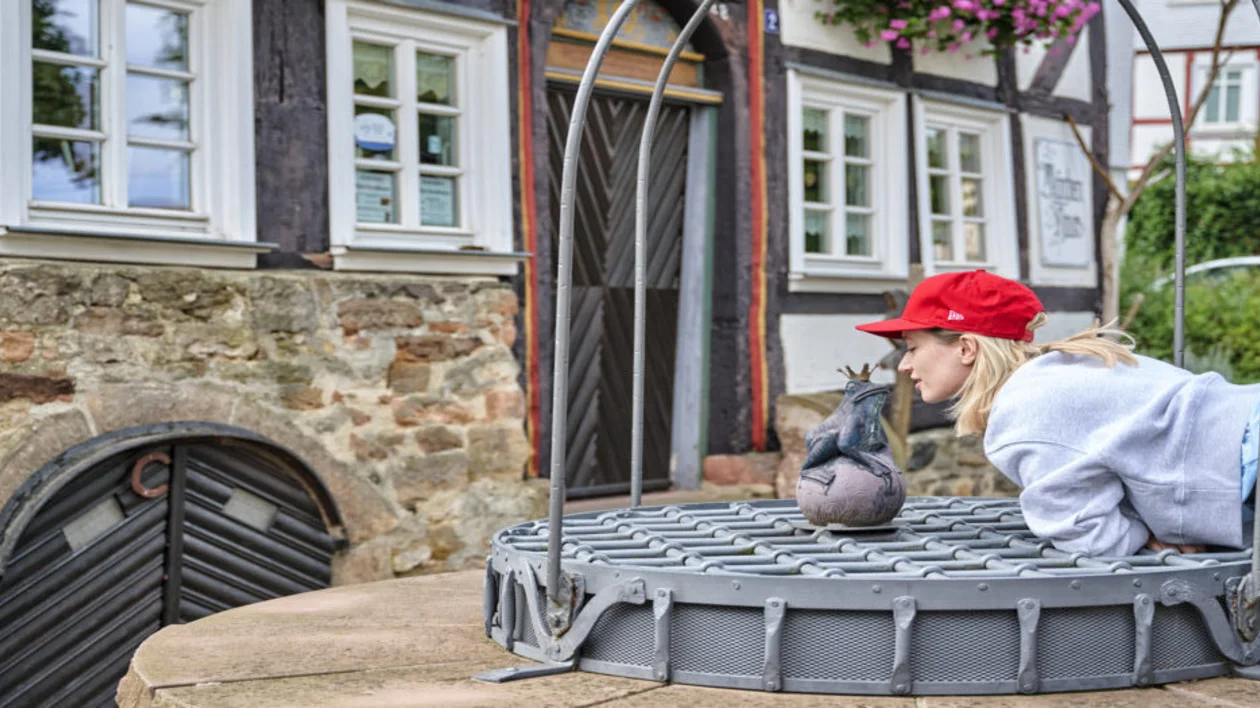 Girl in red cap leaning toward a small bird statue on a metal railing.