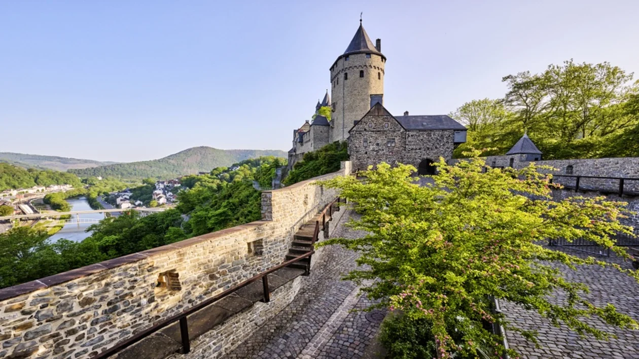Altena Castle overlooking a river valley in Germany, surrounded by stone walls and forested hills in a fairytale setting.