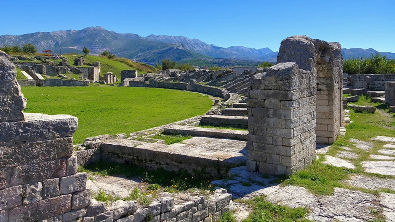 Salona ruins of a Roman amphitheater surrounded by green grass and mountains in Dalmatia.