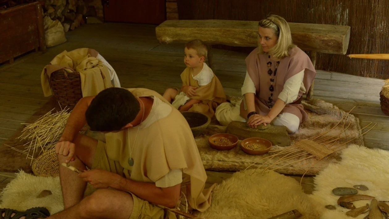 Prehistoric life reenactment in Europe with adults and child crafting tools and preparing food in a traditional setting