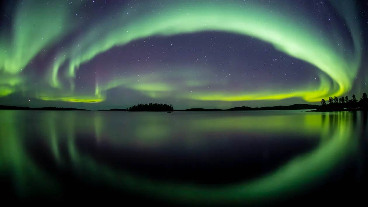 Green and purple aurora borealis reflected over a calm lake at night.