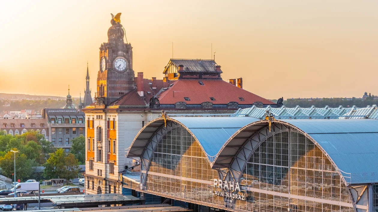 Historic train station with arched glass roofs at sunset, clock tower in the background.
