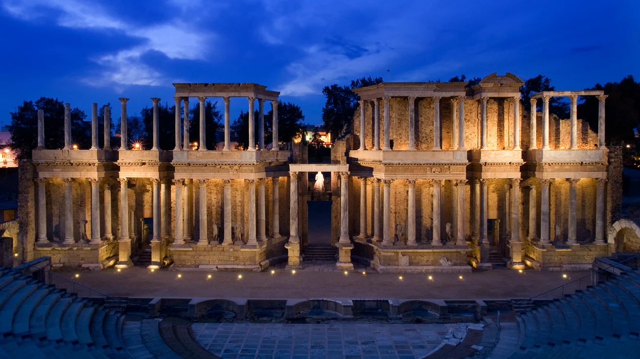 Ancient Roman amphitheater illuminated at dusk with dramatic blue sky overhead.