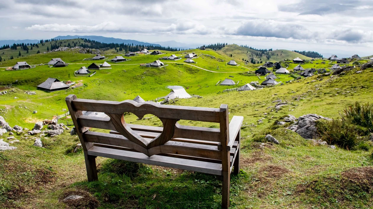 Wooden bench with heart cutout overlooking green hills and scattered houses.