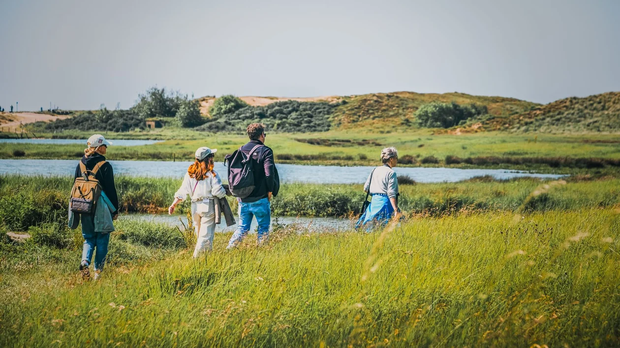 Four people hiking through grassy fields near a river on a sunny day.