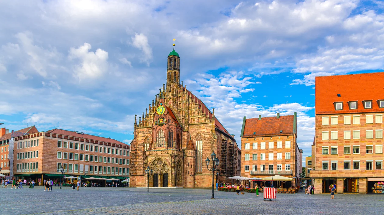Medieval church in a town square with colorful buildings under a blue cloudy sky.