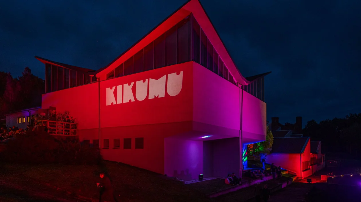Modern building illuminated with red and purple lights at night, "KIKUMU" projected on wall.