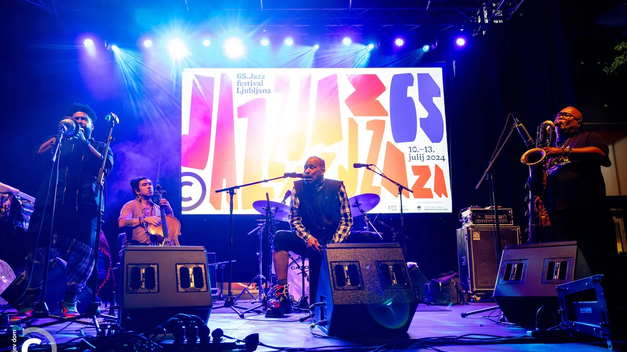 Live band performing on stage with colorful lights and a jazz festival sign behind them.