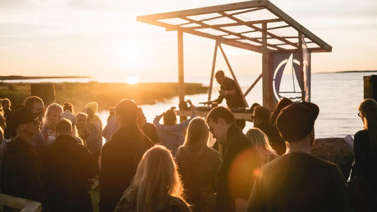 People gathered at an outdoor music event by the water at sunset.