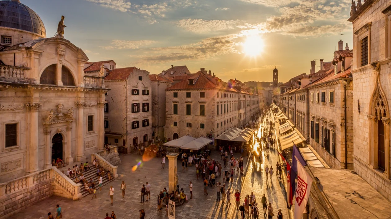 Crowded street with historic buildings at sunset, warm sunlight reflecting off stone walkway.