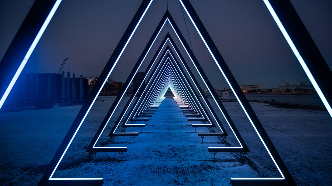 Illuminated triangular arches forming a tunnel over a snowy path at night.