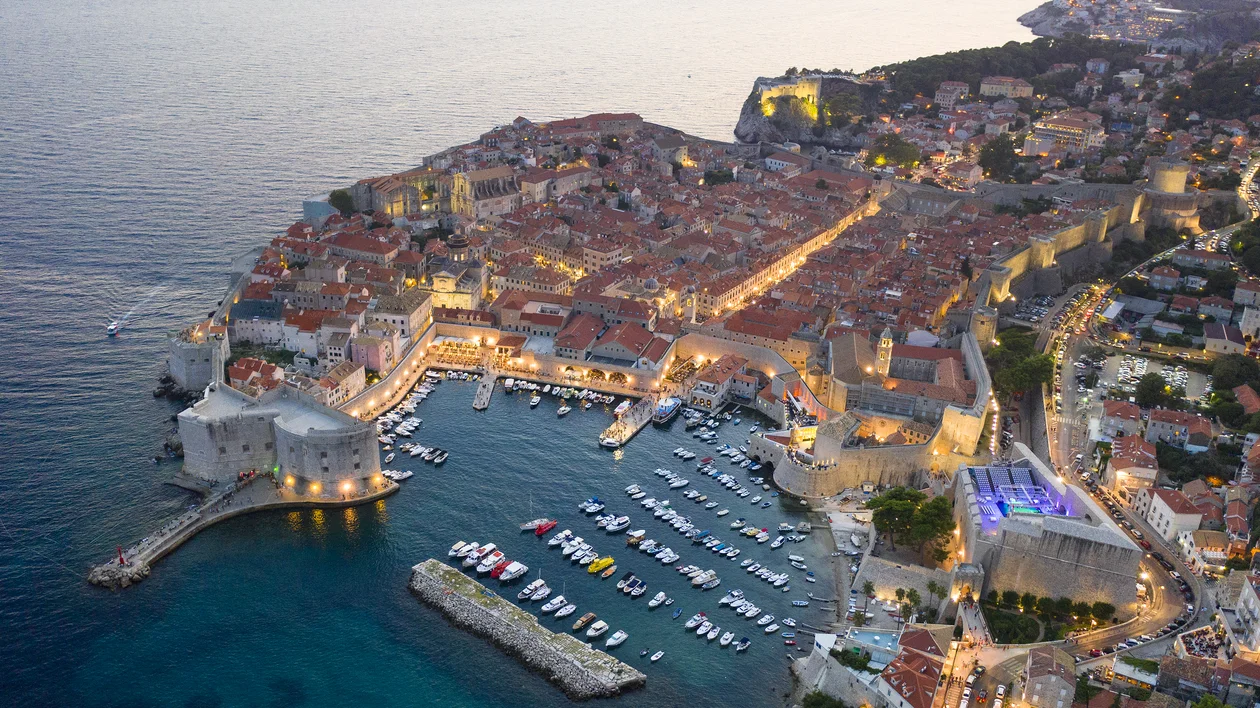 Aerial view of a coastal town with red rooftops and a marina at sunset.