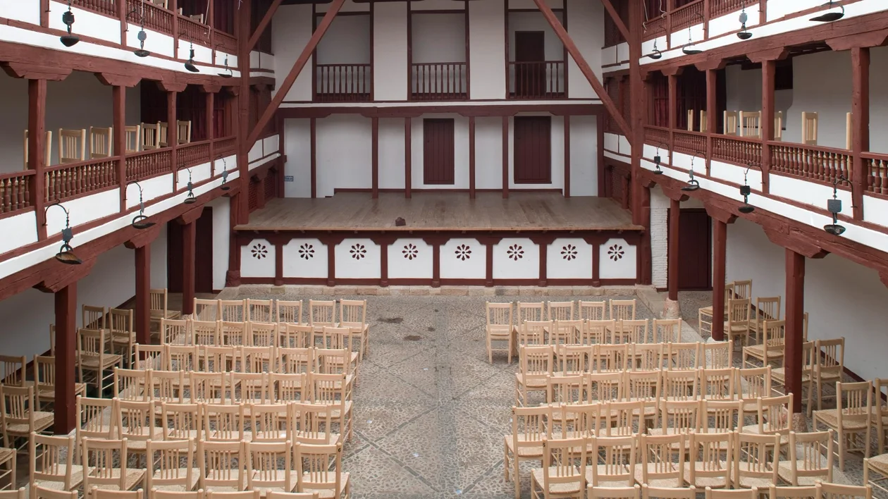 Empty wooden chairs facing a stage in an open-air theater with red and white architecture.