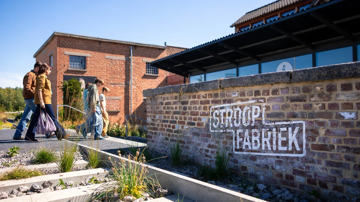 People walking past a brick building with "Stroopfabriek" painted on the wall.