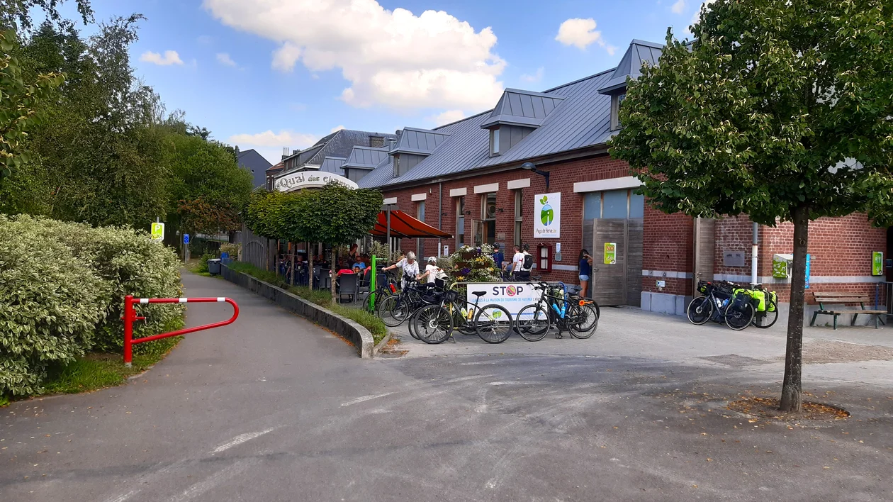 People with bicycles gathered outside a brick building on a sunny day.