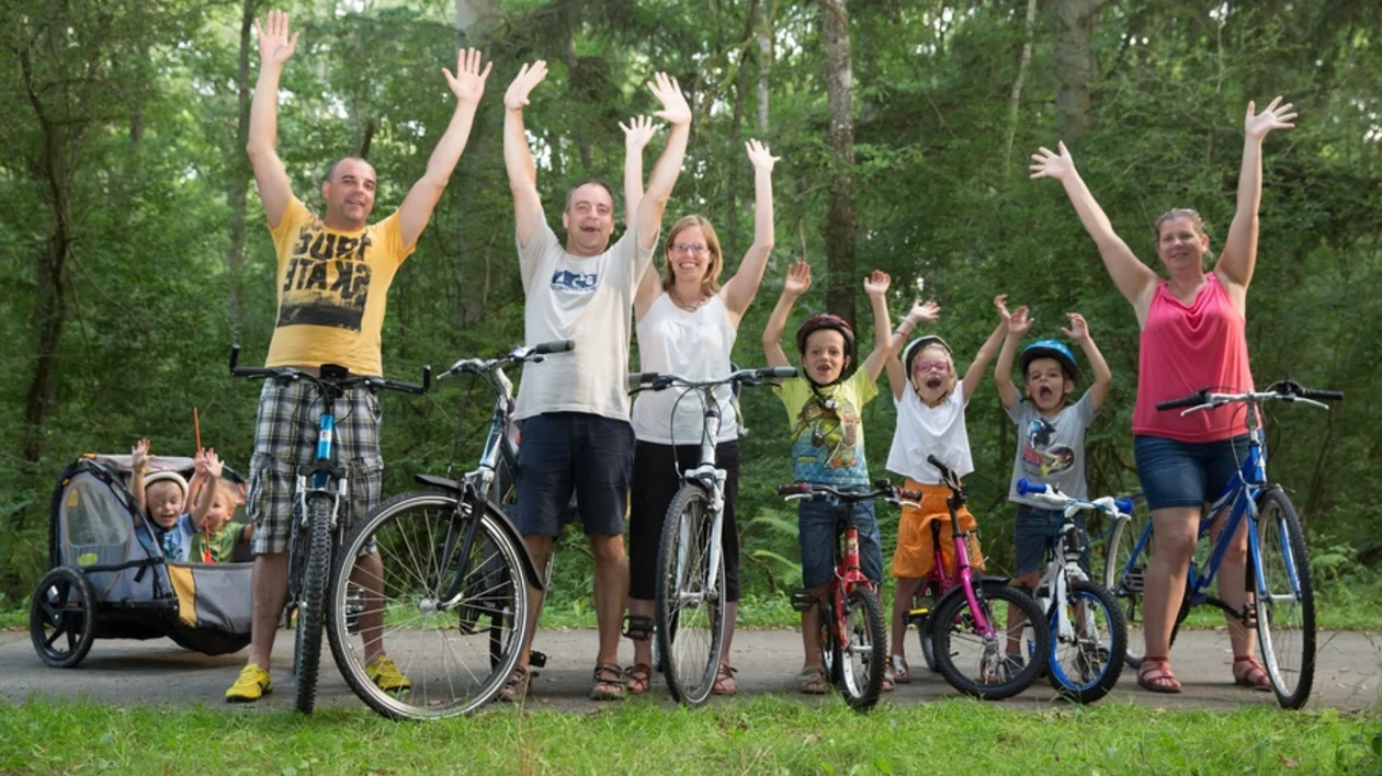Group of happy people with children and bicycles raising their arms in a green forest.
