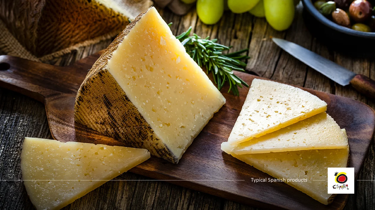 Manchego cheese wedges on a wooden board with grapes, rosemary, and a knife.