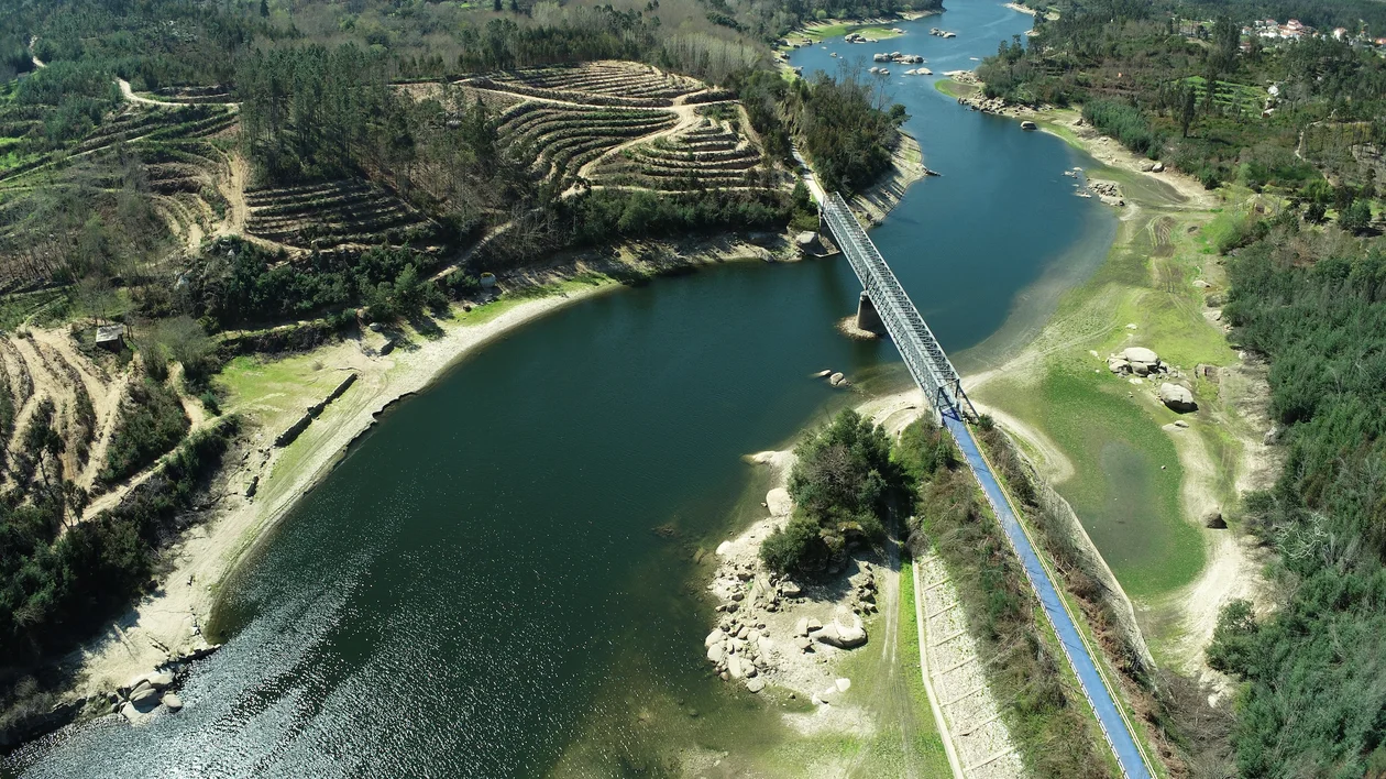 A bridge crosses a winding river surrounded by lush green hills and scattered trees.