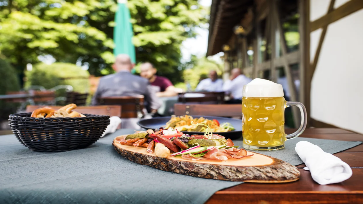 Beer and assorted food on an outdoor table, people sitting in the background.