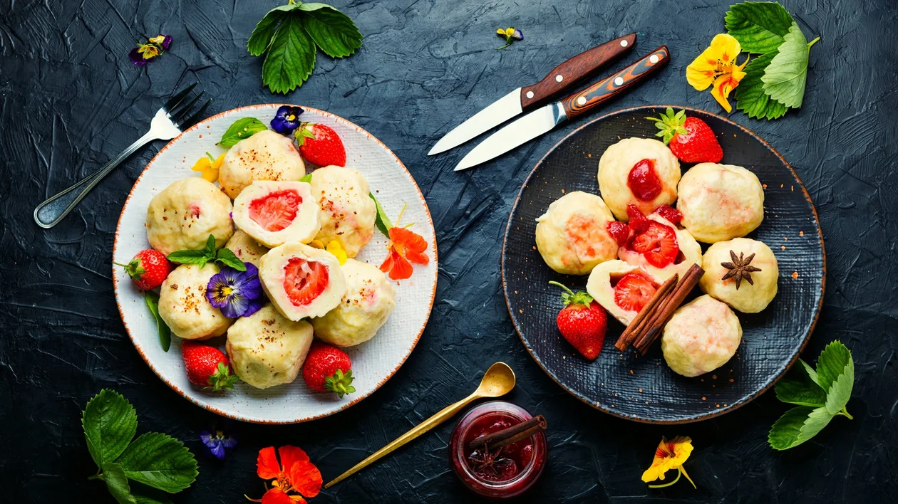 Strawberry dumplings on two plates, garnished with fresh strawberries and edible flowers.