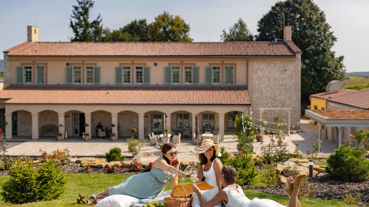 Three women having a picnic on a lawn in front of a large house on a sunny day.