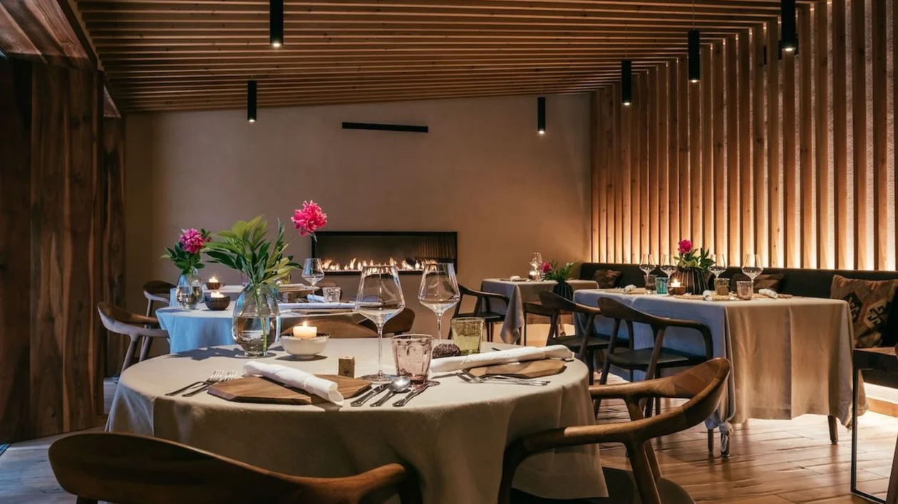 Elegant restaurant with wooden decor, set tables, flowers, and soft ambient lighting.