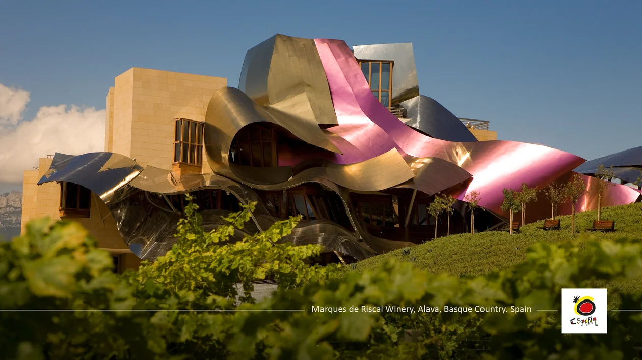 Modern building with curved metallic surfaces and pink accents, surrounded by greenery.