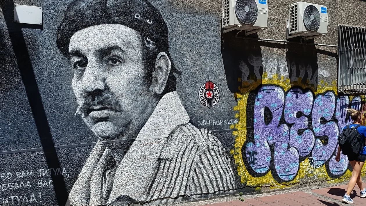 Large mural of a man in a beret beside colorful graffiti on a city wall.