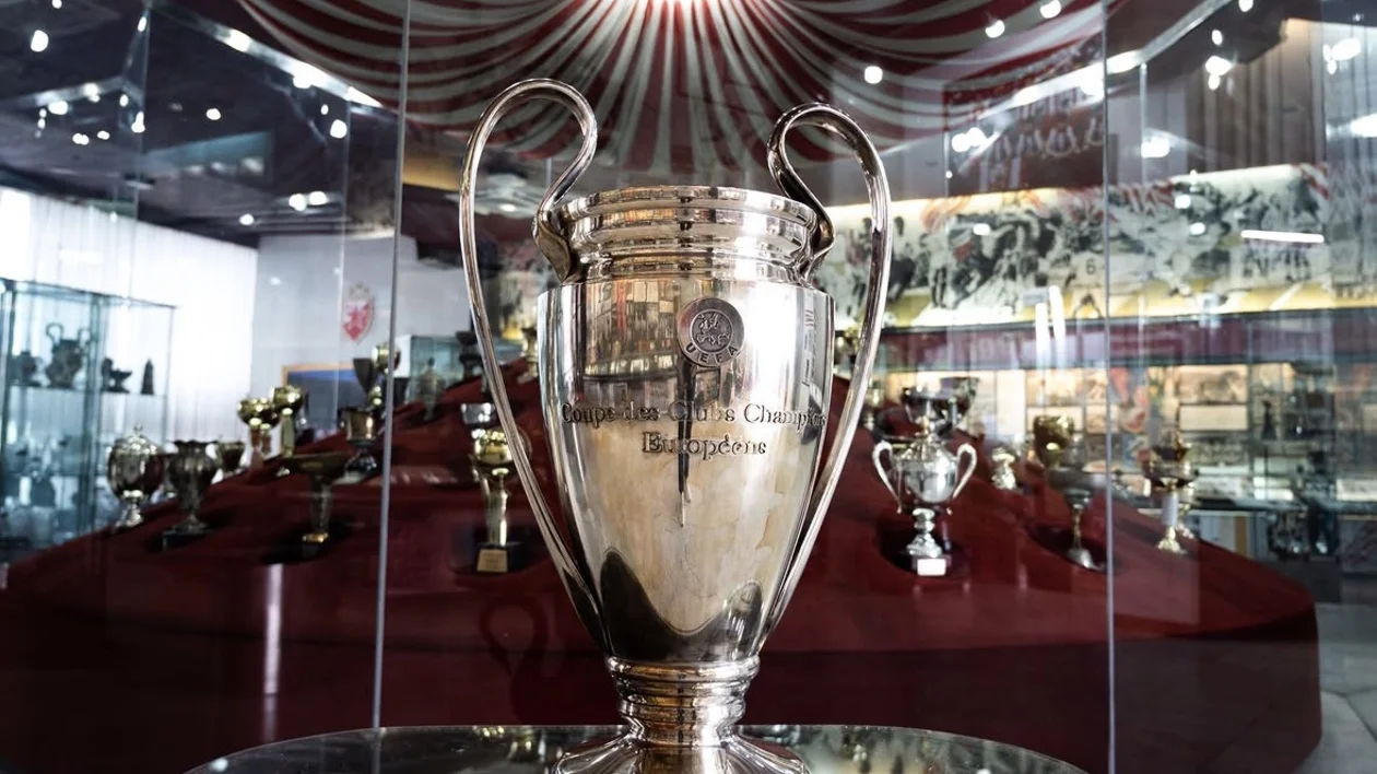 Large silver trophy displayed in a glass case among other trophies in a museum setting.
