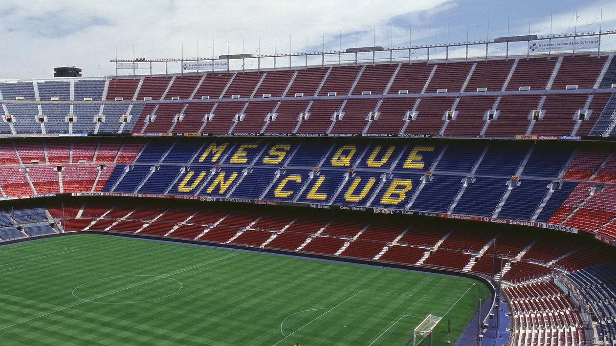 Empty football stadium with seats displaying "MES QUE UN CLUB" in yellow letters.
