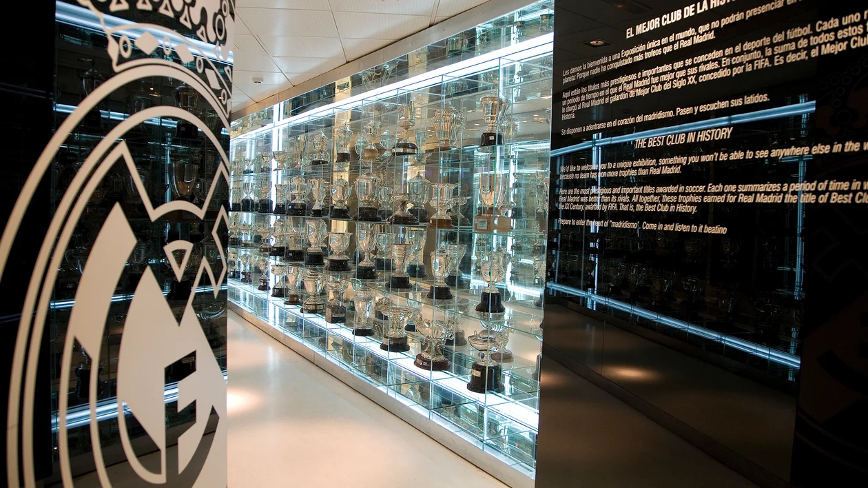 Glass trophy display with Real Madrid logo and illuminated text panels in a modern museum setting.