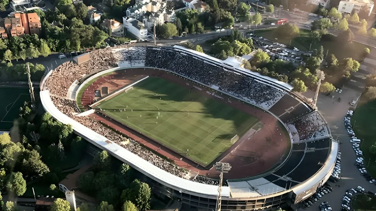 Aerial view of a large stadium surrounded by trees and city buildings.