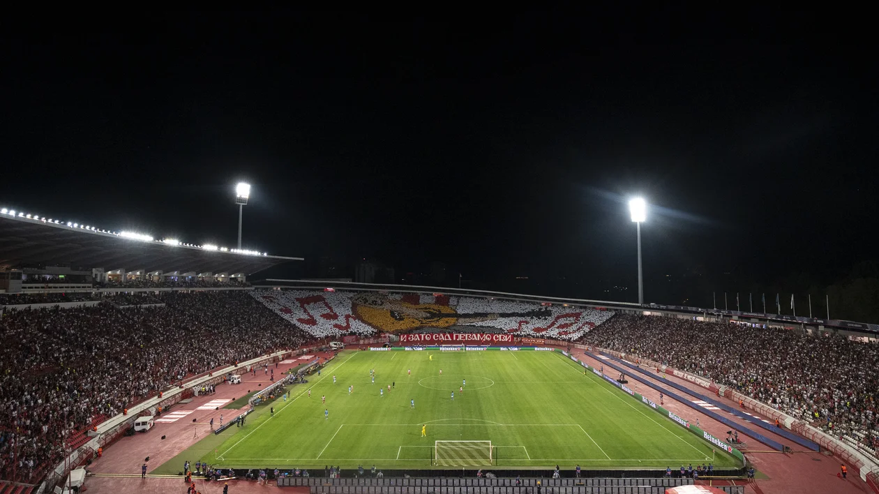 Crowded soccer stadium at night with fans and bright floodlights illuminating the field.