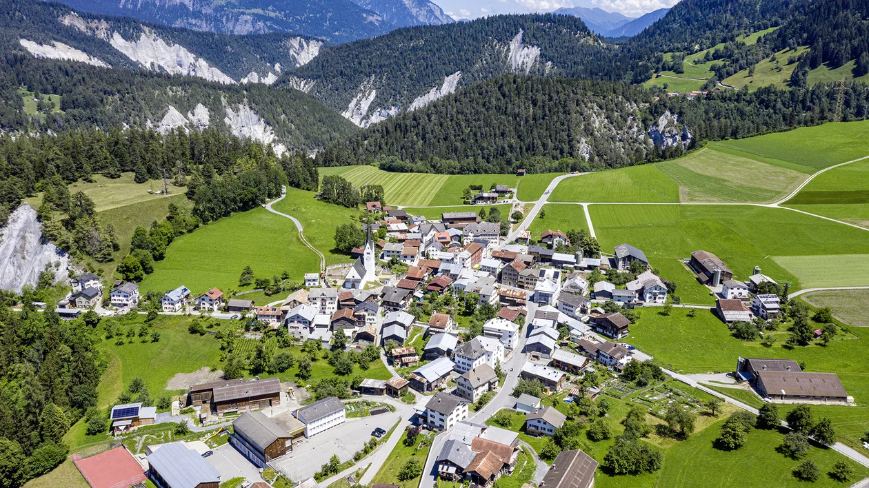 Aerial view of a small village surrounded by green fields and mountains.