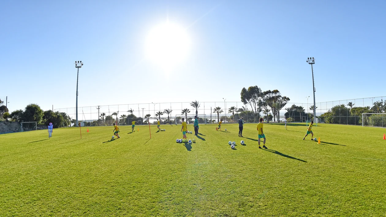 Children playing soccer on a sunny field with bright green grass and clear blue sky.