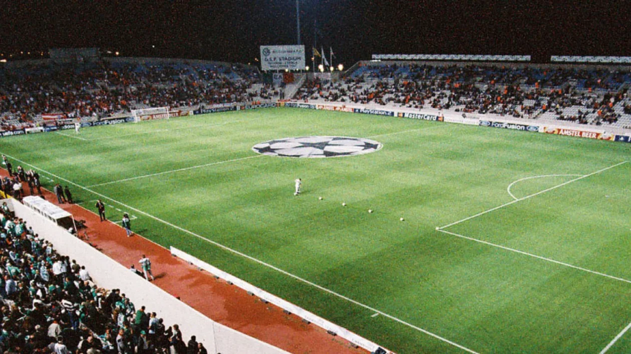 Nighttime soccer stadium with green field and scattered fans in the stands.