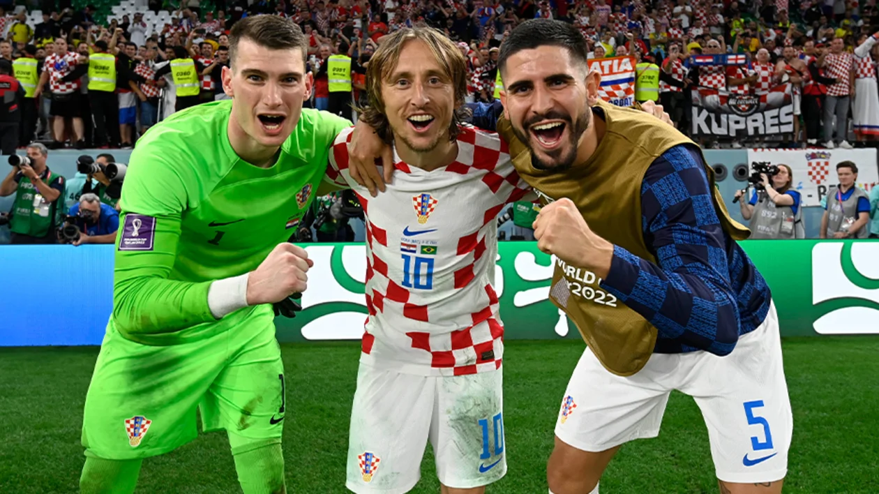 Three Croatian soccer players celebrating on the field, smiling with fists raised.