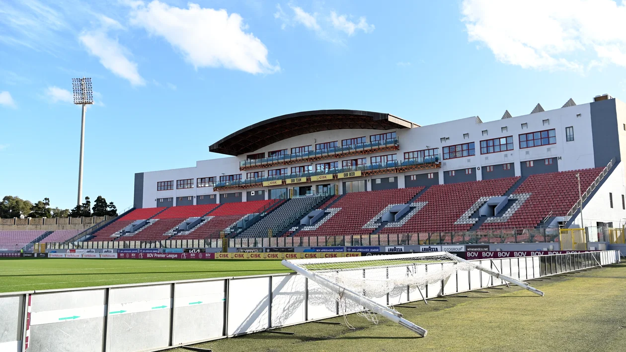 Empty stadium with red and green seats under a blue sky with scattered clouds.