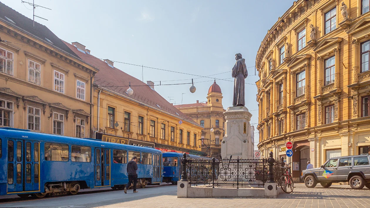 Blue tram passing by a statue in a historic European city square.