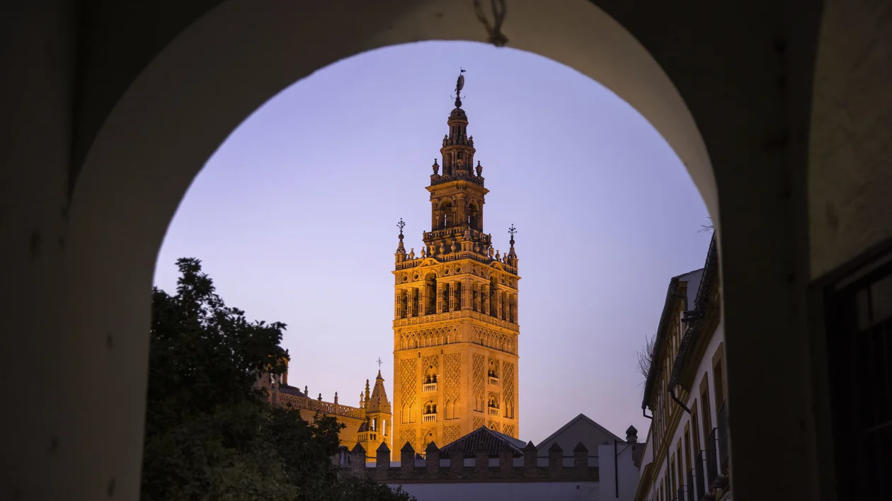 Illuminated tower framed by an arch at dusk, with a clear evening sky.