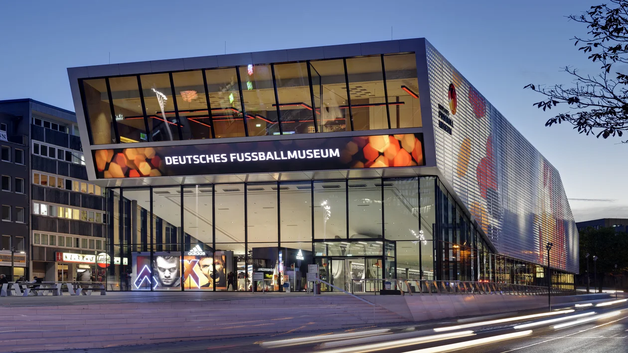 Modern glass building of the German Football Museum lit up in the evening.