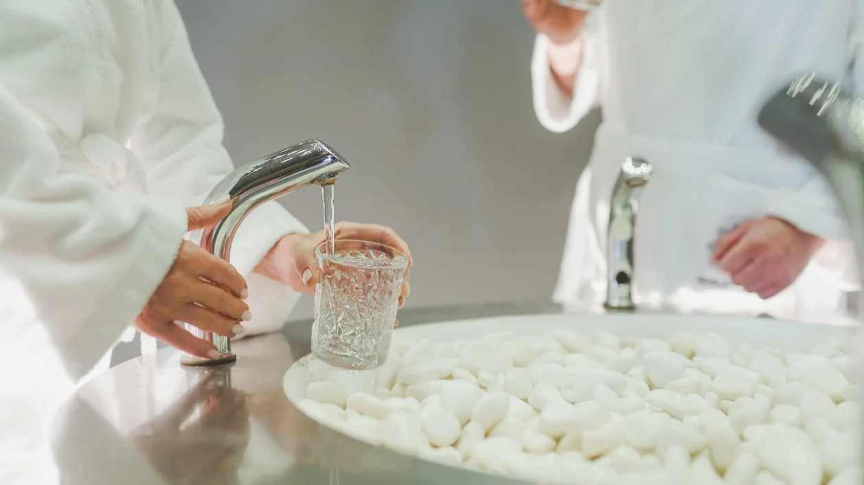 People in white robes filling glasses with water at a spa-like setting.