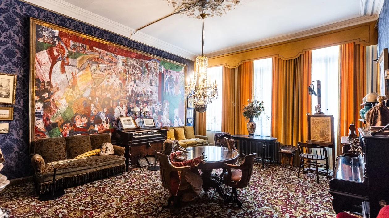 Ornate vintage living room with patterned walls, colorful carpet, and large mural.