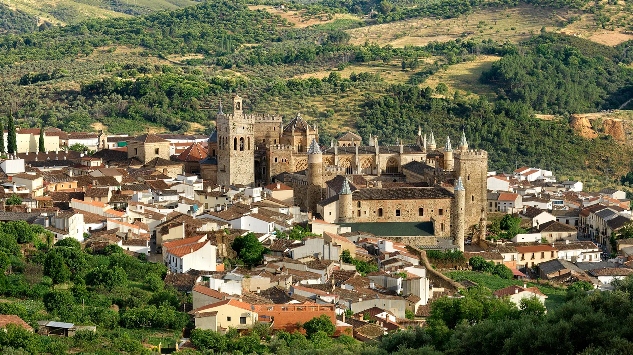 Historic stone monastery surrounded by village rooftops and green hills.