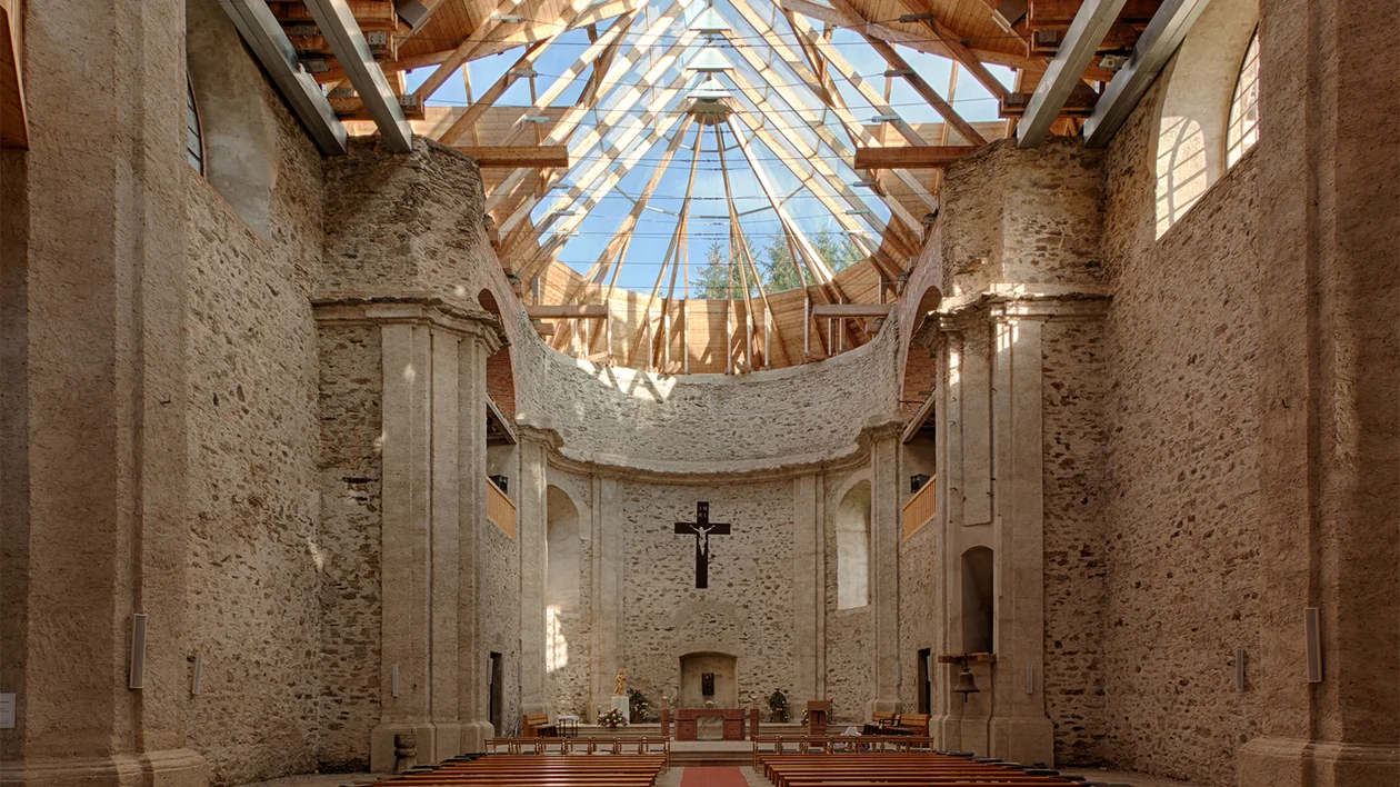 Church interior with stone walls, wooden benches, and a glass roof letting in sunlight.