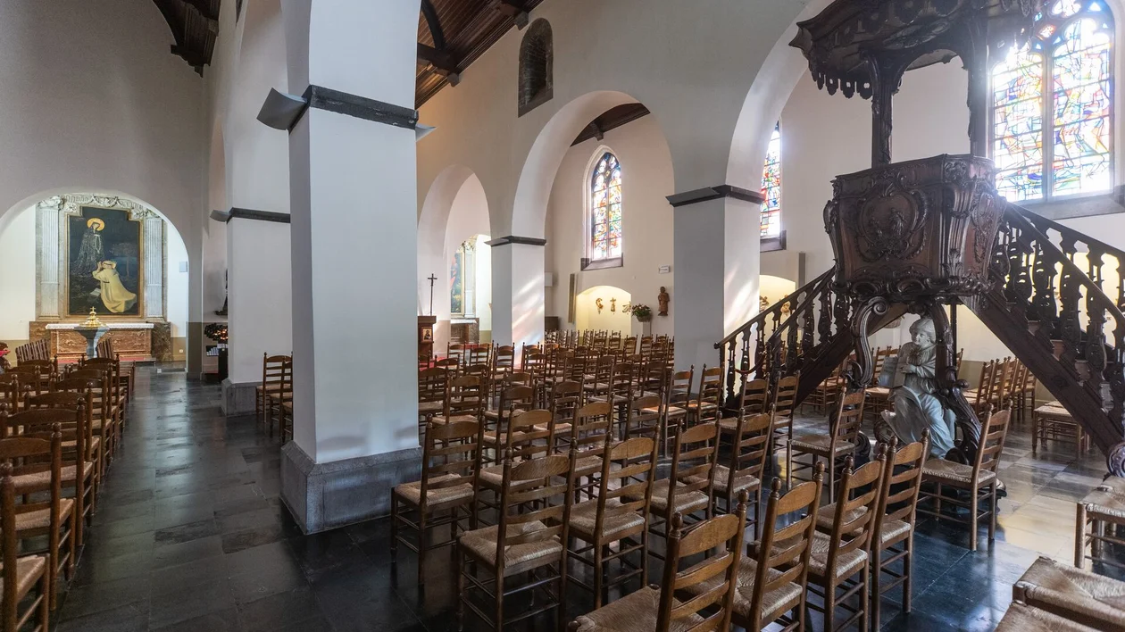 Wooden chairs and a large pulpit inside a church with stained glass windows.