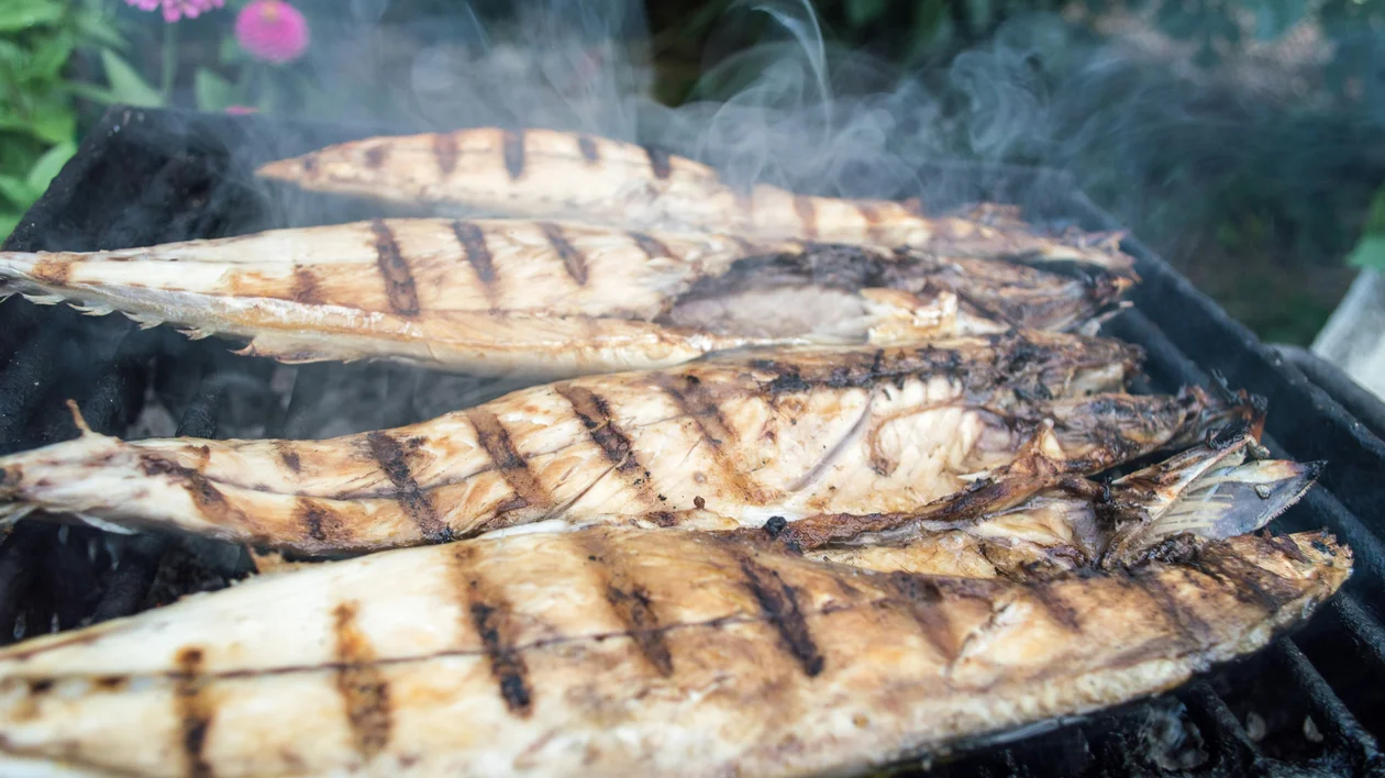 Grilled fish fillets with char marks cooking on a smoky outdoor barbecue.