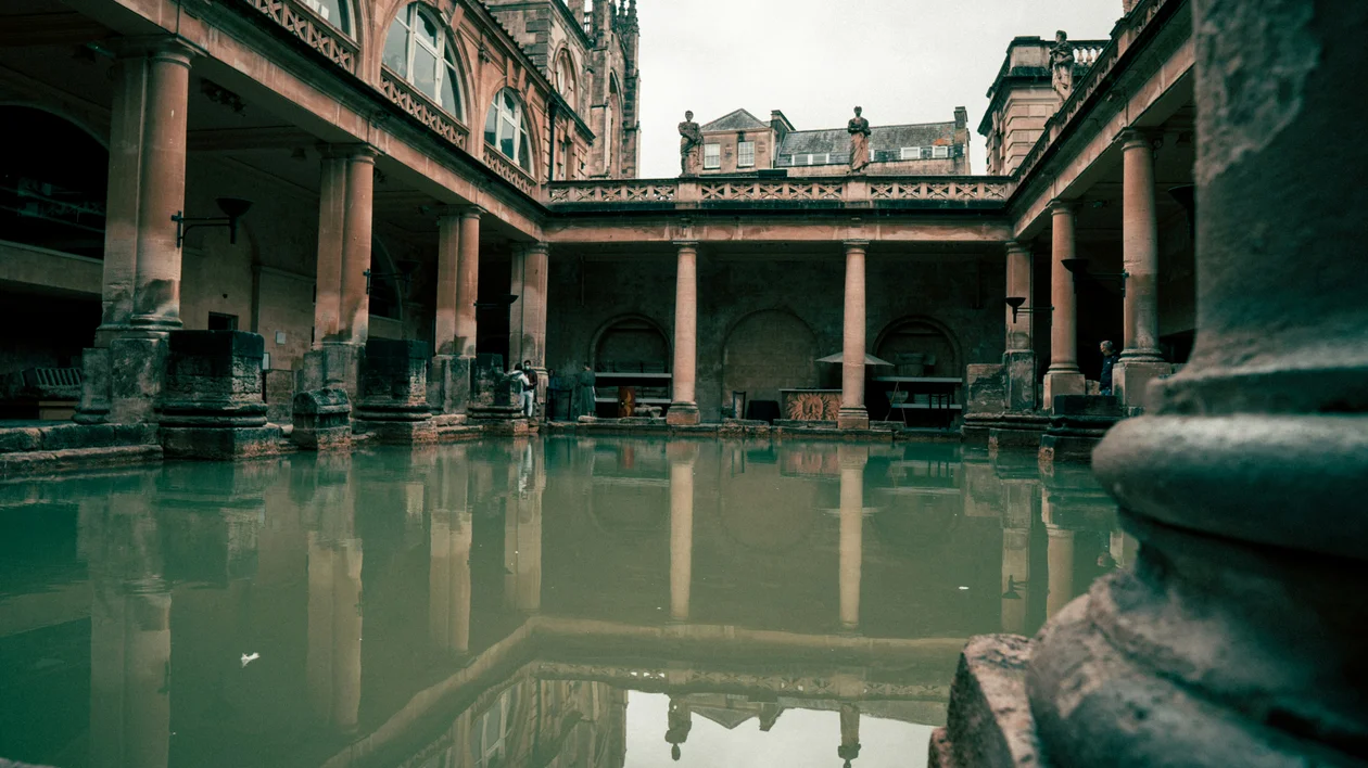 Ancient Roman bath with green water surrounded by stone columns and arches.