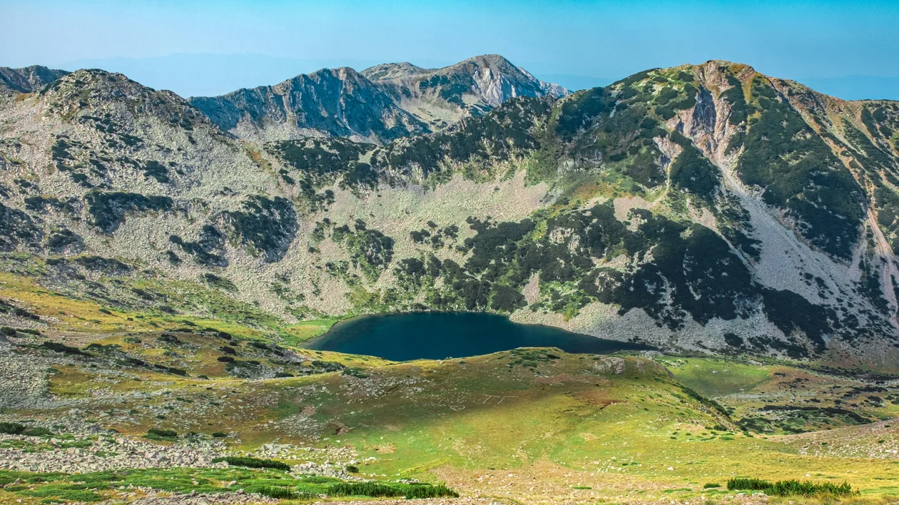 Mountain landscape with a small lake at the base, under a clear blue sky.